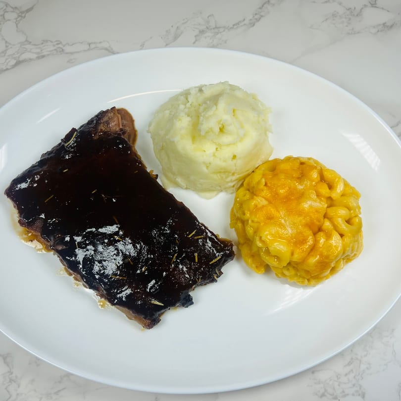 A plate of BBQ ribs with mashed potatoes and macaroni and cheese on a white plate.