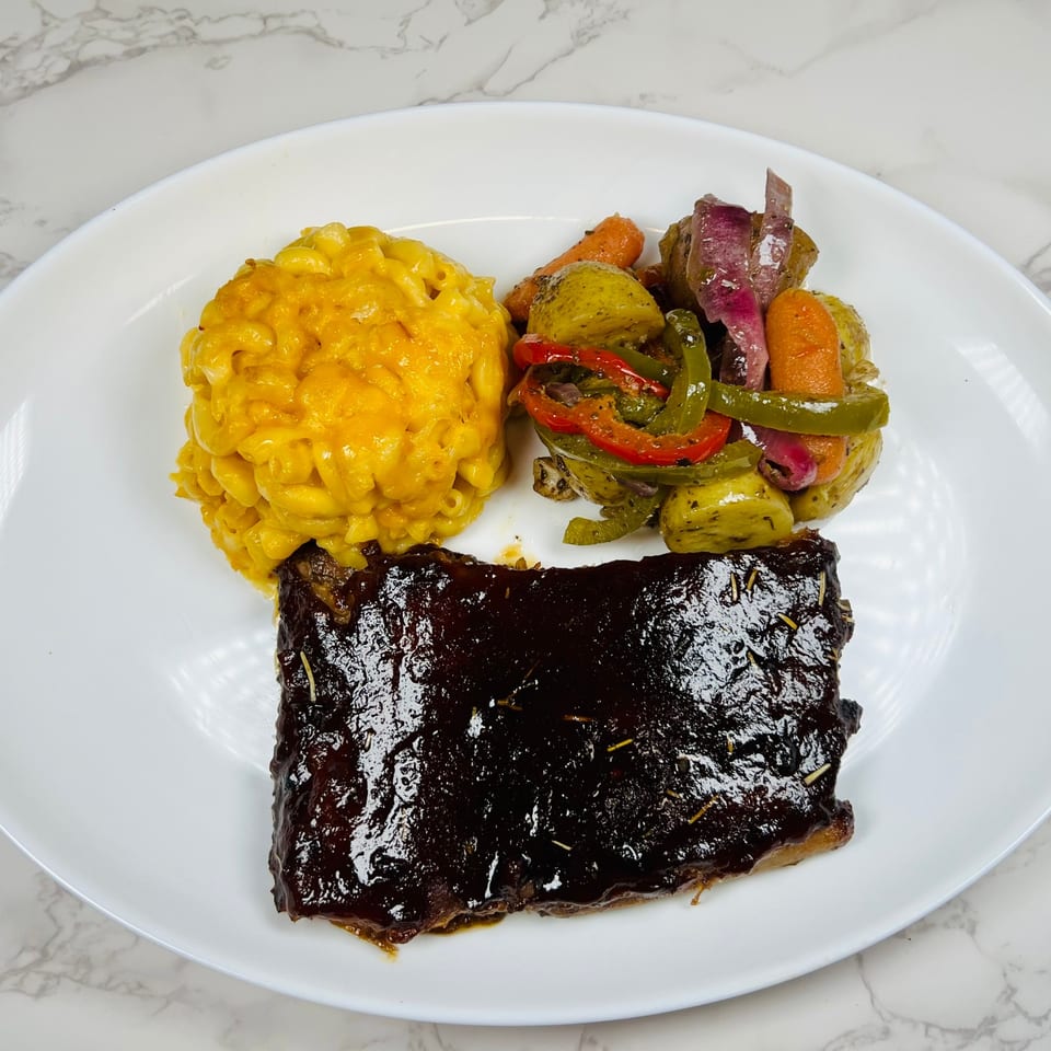 A plate of BBQ ribs, macaroni and cheese, and roasted vegetables on a white plate.