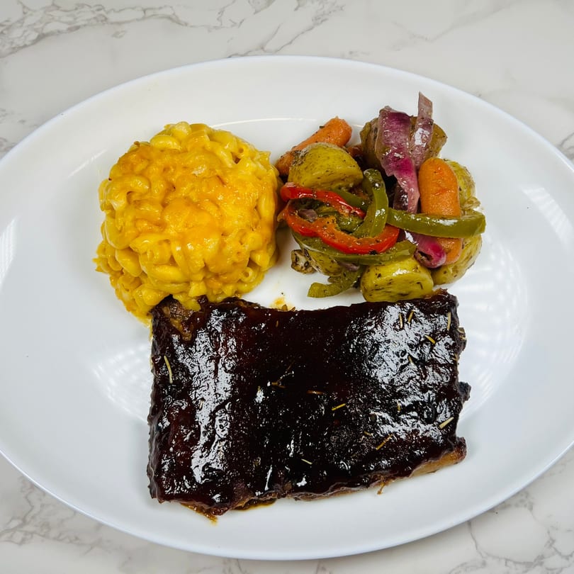 A plate of BBQ ribs, macaroni and cheese, and roasted vegetables on a white plate.